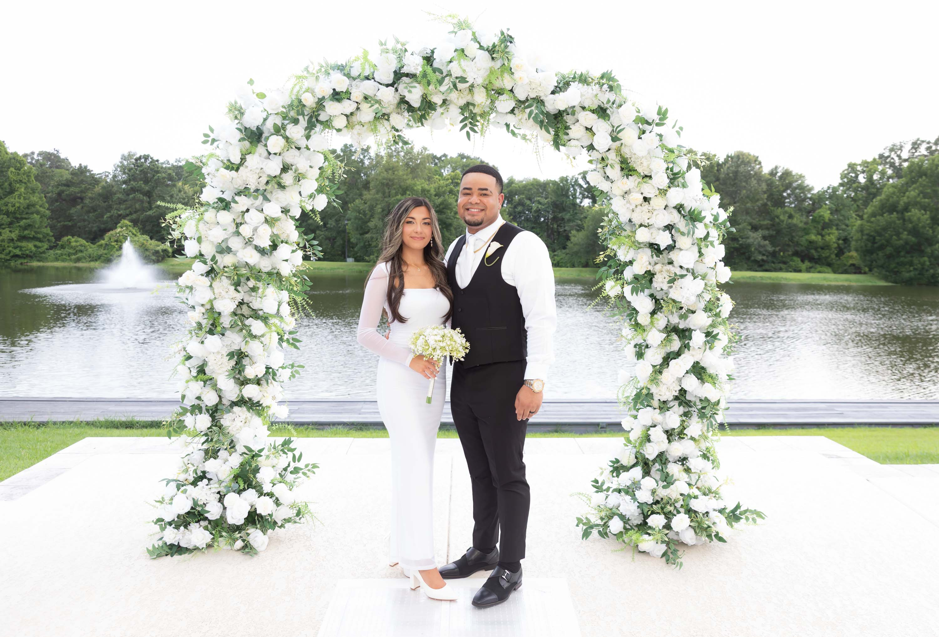 Newly married Nano Nuptials couple beneath the floral arch by the lake